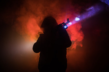 Silhouette of man with assault rifle ready to attack on dark toned foggy background or dangerous bandit in black wearing balaclava and holding gun in hand. Shooting terrorist with weapon theme decor