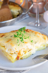 Piece of cheesy scalloped potatoes or potato gratin on plate, holiday theme, vertical