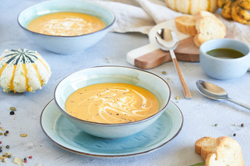 Pumpkin soup in plates with French baguette and cream on a light gray background. Autumn composition. Two plates of soup
