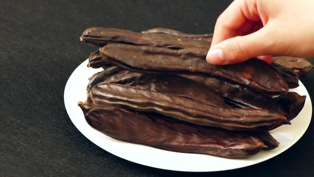 carob fruit of a man's hand, carob on a plate, on a white background