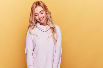 Obraz premium Cute woman with long blond wavy hair dressed in light pink sweater standing on yellow background with her eyes closed
