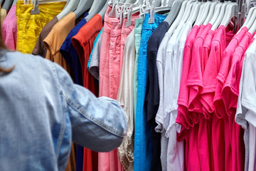 Hangers with clothes in the store. Large selection of women's clothing. Sale of female trousers and T-shirts