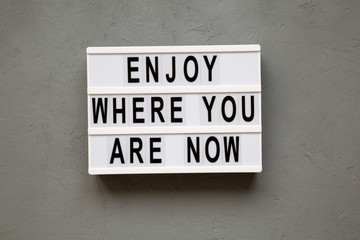'Enjoy where you are now' words on modern board over concrete background, top view. Flat lay, from above.