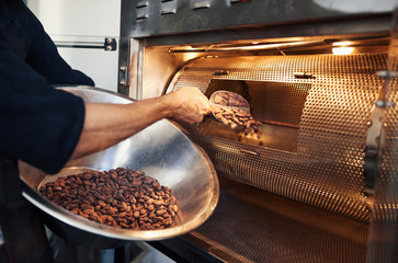 Chocolate making factory worker putting cocoa beans into a roaster