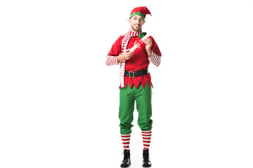 smiling man in christmas elf costume holding wishlist roll and looking at camera isolated on white