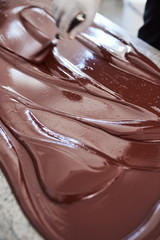 Worker spreading melted artisanal chocolate out on a factory table