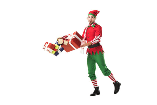 surprised man in christmas elf costume accidentally dropping pile of presents isolated on white