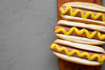 Homemade hot dogs with yellow mustard on wooden board over concrete background, top view. Flat lay,...