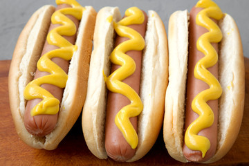 Tasty hot dogs with yellow mustard on wooden board on grey background, side view. Close-up.