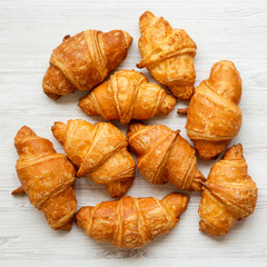 Freshly baked golden croissants on white wooden background, overhead view. Close-up.