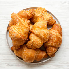 Fresh croissants on grey round plate on white wooden table, overhead view. From above, flat lay, top view.