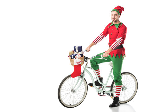 Man In Christmas Elf Costume Riding Bike With Basket Full Of Presents Isolated On White