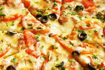 Hot pizza with cheese, ham and chicken, fresh tomato slices and olives cutted to pieces, side view. Could be used as food background or in restaurant menu