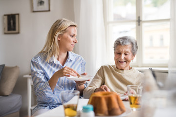 Senior woman in wheelchair with a health visitor sitting at the table at home, eating.