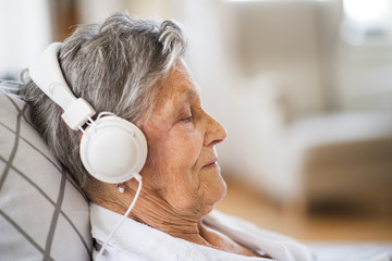 Sick senior woman with headphones lying in bed at home or in hospital.