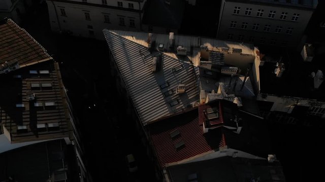 Światła jadącego samochodu na tle ciemnej ulicy podczas zachodzącego słońca. Dachy kamienic.
