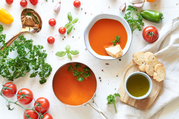 Gazpacho soup in metal pan and plate with fresh tomatoes, green sauce, chili, garlic, Basil and French baguette on white background. Top view