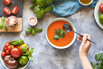 Gazpacho soup in a plate with fresh tomatoes, green sauce, chili, garlic, Basil and French baguette on a gray background. Top view