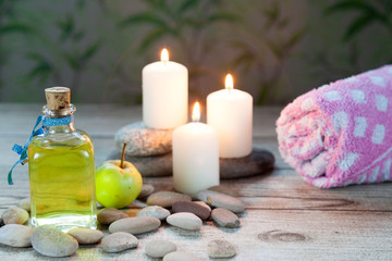bottle of  oil massage, river pebbles and a small green apple
