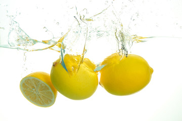 Three ripe lemons spash in water on white