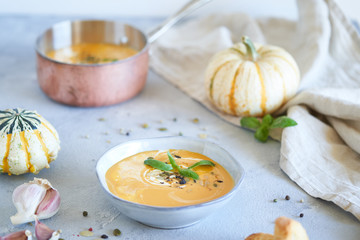 Pumpkin soup in plates with French baguette and cream on a light gray background. Autumn composition. One plate of soup and a copper pot