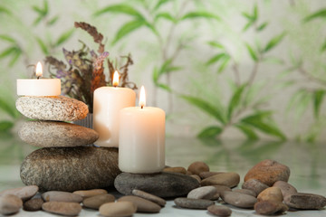Fototapeta na wymiar Three lighted candles on river pebbles with lavender on herbal background