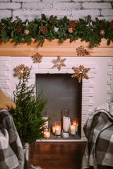 Decorative fireplace decorated with New Year's garland and burning candles in glass cups. Cozy Christmas atmosphere.