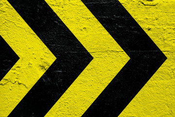 Warning sign yellow and black stripes as arrows painted over concrete cement wall as texture...