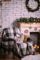 Armchair covered with a cozy blanket, standing near the fireplace decorated with a Christmas garland.