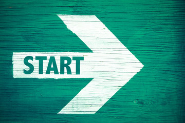 Start text written on white directional arrow pointing right painted on a green wooden signboard background. Motivation concept for start line for business begin and professional career path.