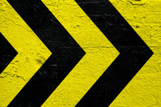 Warning sign yellow and black stripes as arrows painted over concrete cement wall as texture background. Concept sign for do not enter the area, caution, danger, hazard.