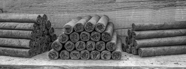 Cigars lie stacked on a wooden table in several blocks. View in black and white. Concept: cigars or...