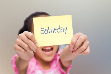 little girl show yellow note with saturday word