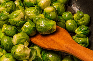 Close up. Small green cabbages of Brussels sprouts are stirred with a spatula in a frying pan.