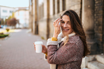 Gorgeous brunette walking in the city and drinking coffee. - obrazy, fototapety, plakaty