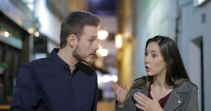 Front view of an angry couple arguing in the night walking towards camera in the street