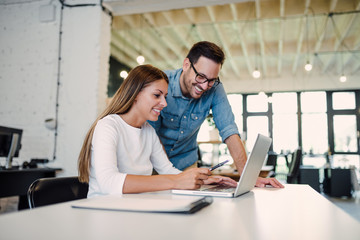 Two young business colleagues using a laptop and talking in a modern office.