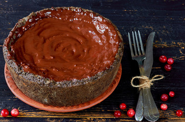Homemade chocolate tart decorated with cranberry, vintage knife and fork on the dark wooden background. Delicious winter dessert for Christmas holidays. Side view