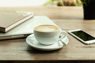 Coffee cup with laptop computer and cell phone on wooden table.