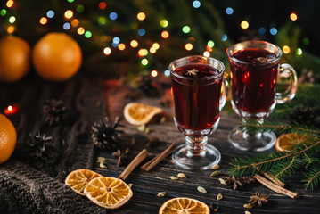 glasses with mulled wine on a wooden table decorated with a Christmas tree and Christmas lights. Traditional winter alcoholic drink with orange slices, cinnamon, cardamom