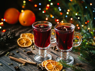 mulled wine in glasses on the table decorated with a Christmas tree. Orange slices, anise stars, cardamom, cinnamon and cloves