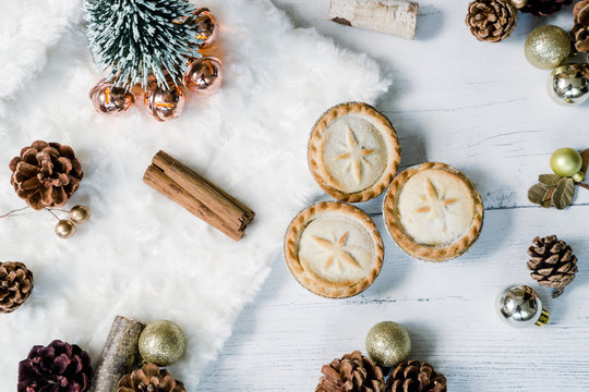Mince pies and cinamon sticks. Christmas tree with golden baubles and pine cones on a white background. Cozy winter flat lay image.