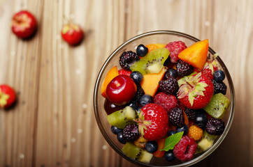 Top view of assorted fruits in glass bowl on kitchen wooden table
