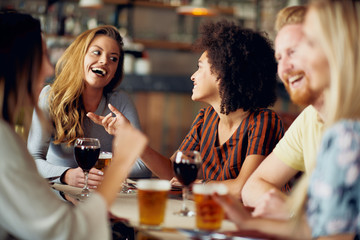 Friends chatting and drinking alcohol while  sitting at restaurant. Multi ethnic group.