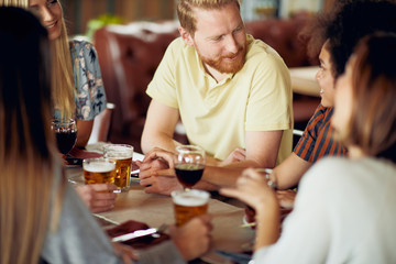 Friends chatting and drinking alcohol while  sitting at restaurant. Multi ethnic group.