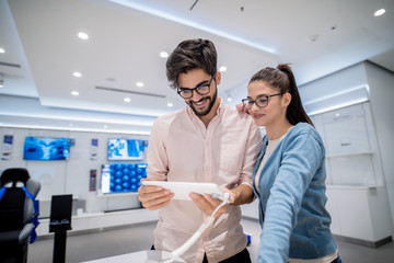 Man holding tablet and woman leaning on man. In background TV screens.