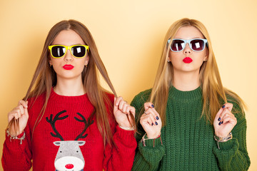 Two funny beautiful hipster girls in sweaters and sunglasses kissing. Concept winter and fashion