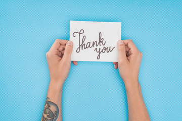 cropped person holding paper with thank you lettering isolated on blue background