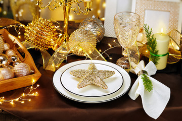 Christmas dinner background, plate, fork, knife and festive decoration on dark rustic wooden table, top view. Table setting and golden holiday decorations, top view. Preparation for Christmas dinner. 