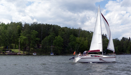 White boat sailing on the lake near Mikolajki, Poland under a cloudy sky. 